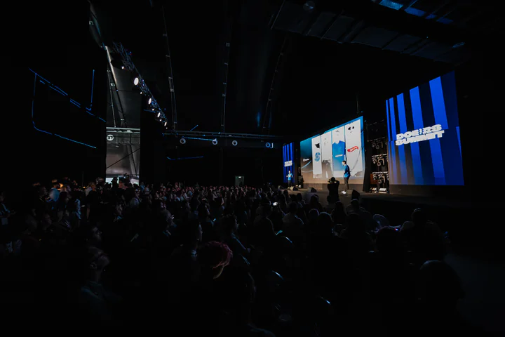 A full Doers Summit auditorium in the dark, facing a blue-lit stage