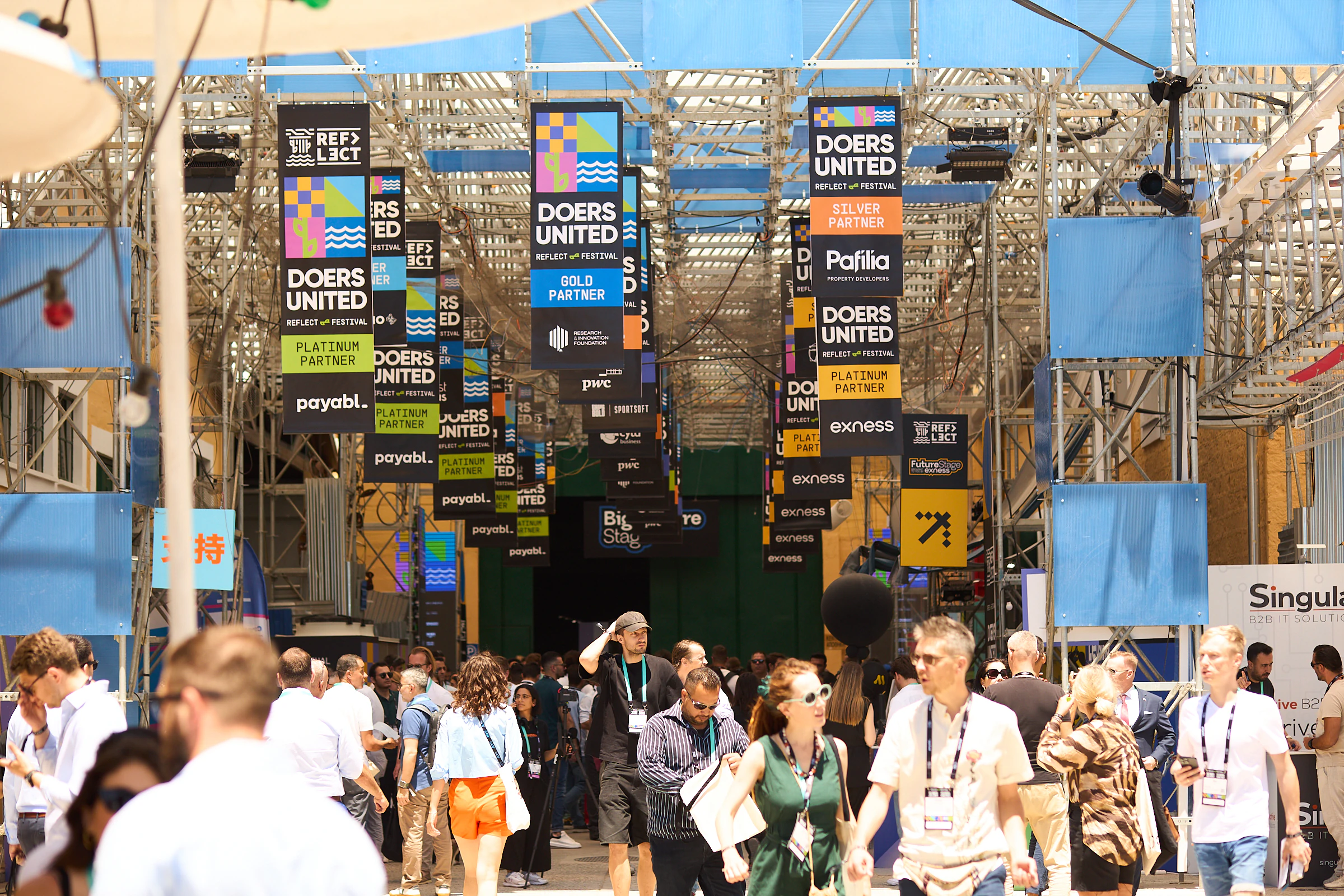 The Doers United expo boulevard under a canopy of partner banners, packed with attendees