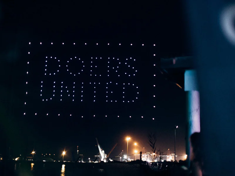 A drone show spelling out Doers United over the water at night
