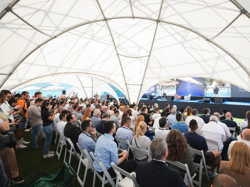 A seated audience under the white tent canopy, facing the Old Port Stage