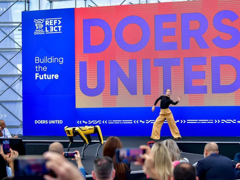 A speaker crossing the main stage in front of a Doers United “Building the Future” wall